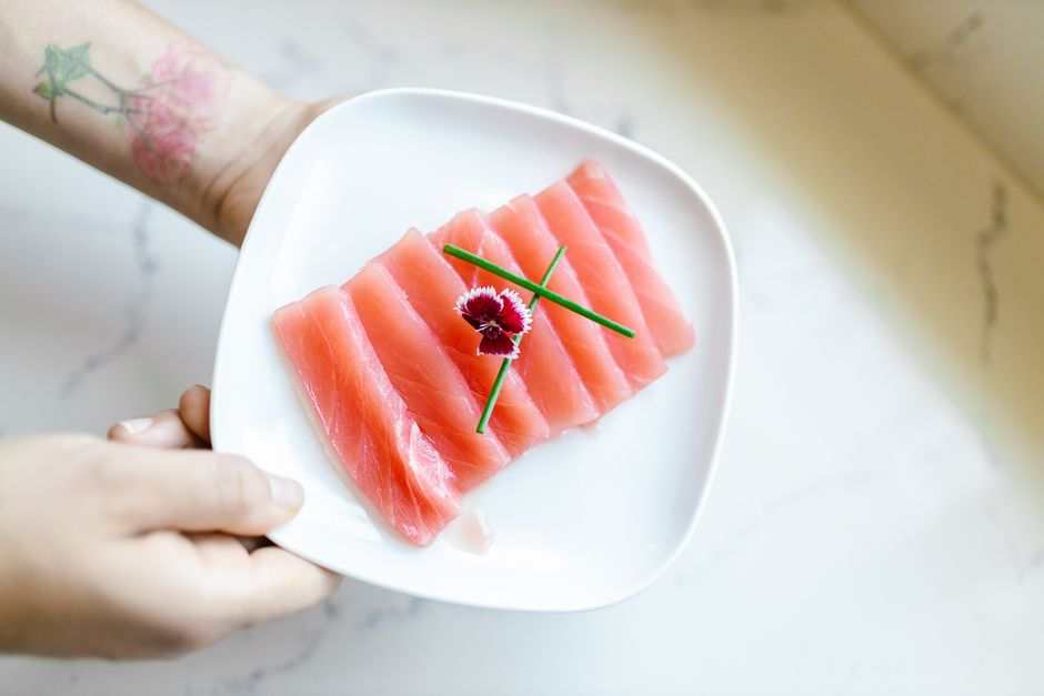 手で持った白い皿に並べたマグロの刺身