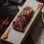 ごま衣をまとわせて表面を炙った赤身魚のたたきを、木製の角皿に並べた盛り付け