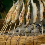 小魚を串に刺し、ひれに白い化粧塩をつけて藁の台に並べ炭火で焼き上げている様子