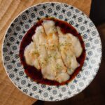 ポン酢だれで和えた白い海鮮の薄切りを柄入りの皿に盛り付けた様子
