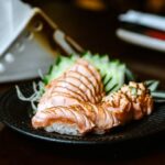 黒い皿に盛った、表面を炙ったサーモンの握り寿司2貫と薬味