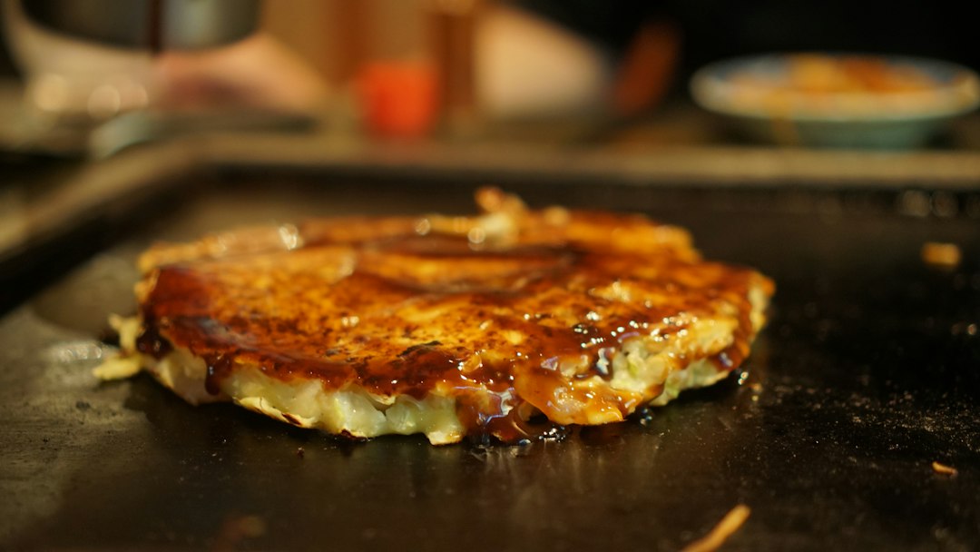 鉄板で焼いたお好み焼きに自家製ソースをかけている様子