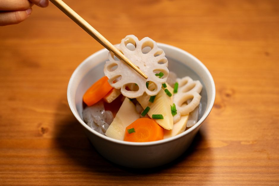 蓮根などの煮物を箸でつまむ小鉢